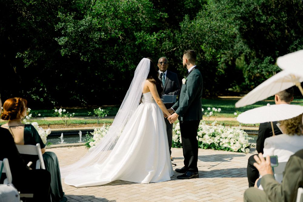 A beautiful outdoor wedding ceremony with the couple exchanging vows on a stone patio surrounded by lush greenery.