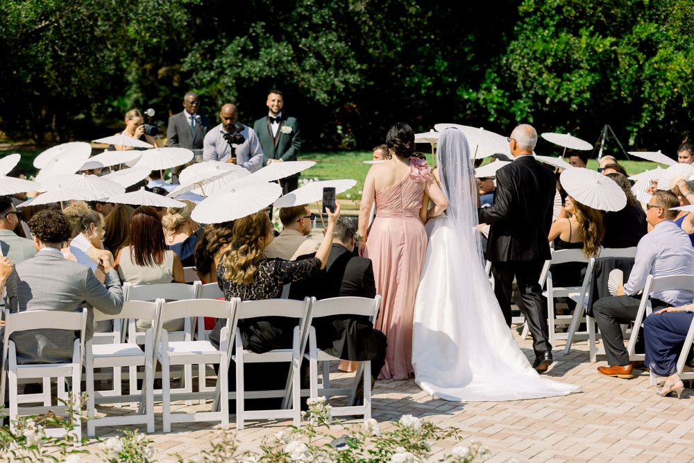 Outdoor wedding ceremony with white umbrellas and folding chairs in a garden setting.