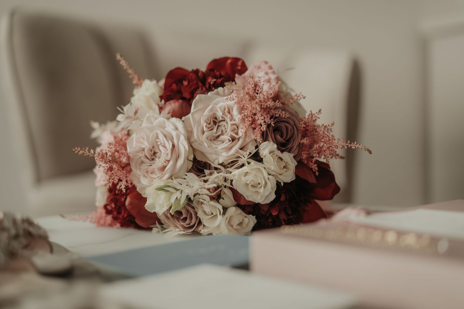 Romantic wedding bouquet featuring blush roses and deep red flowers on a light surface.