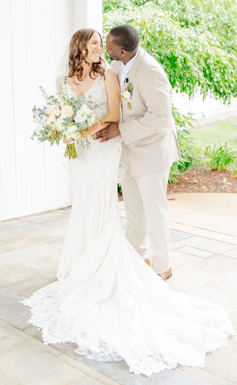 A romantic wedding portrait shows couple embracing with bride holding elegant pastel bouquet.