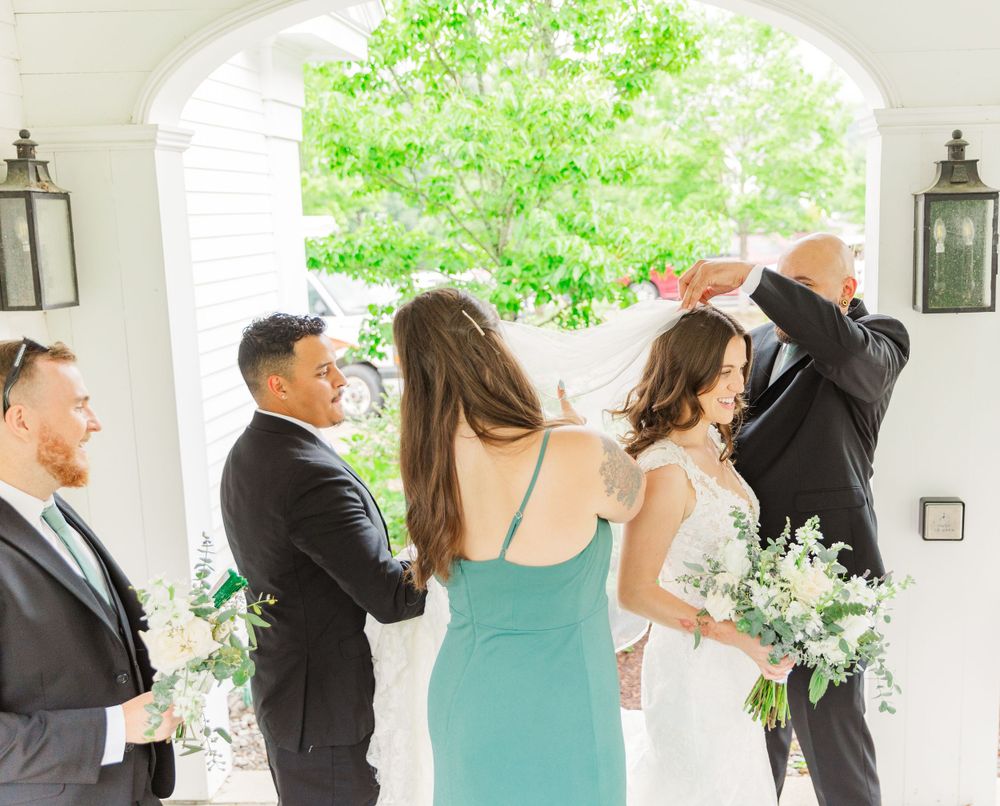Wedding party members gather under a white archway wearing formal attire with mint green dresses and black suits.