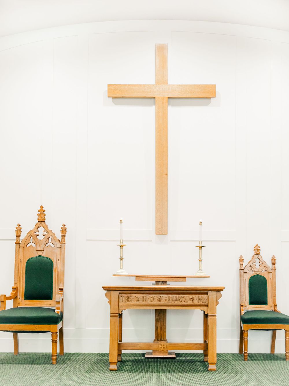 Church altar setup with wooden cross and ornate green chairs for wedding ceremony.