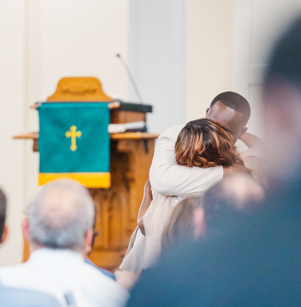 Emotional embrace during church ceremony with green altar cloth visible.