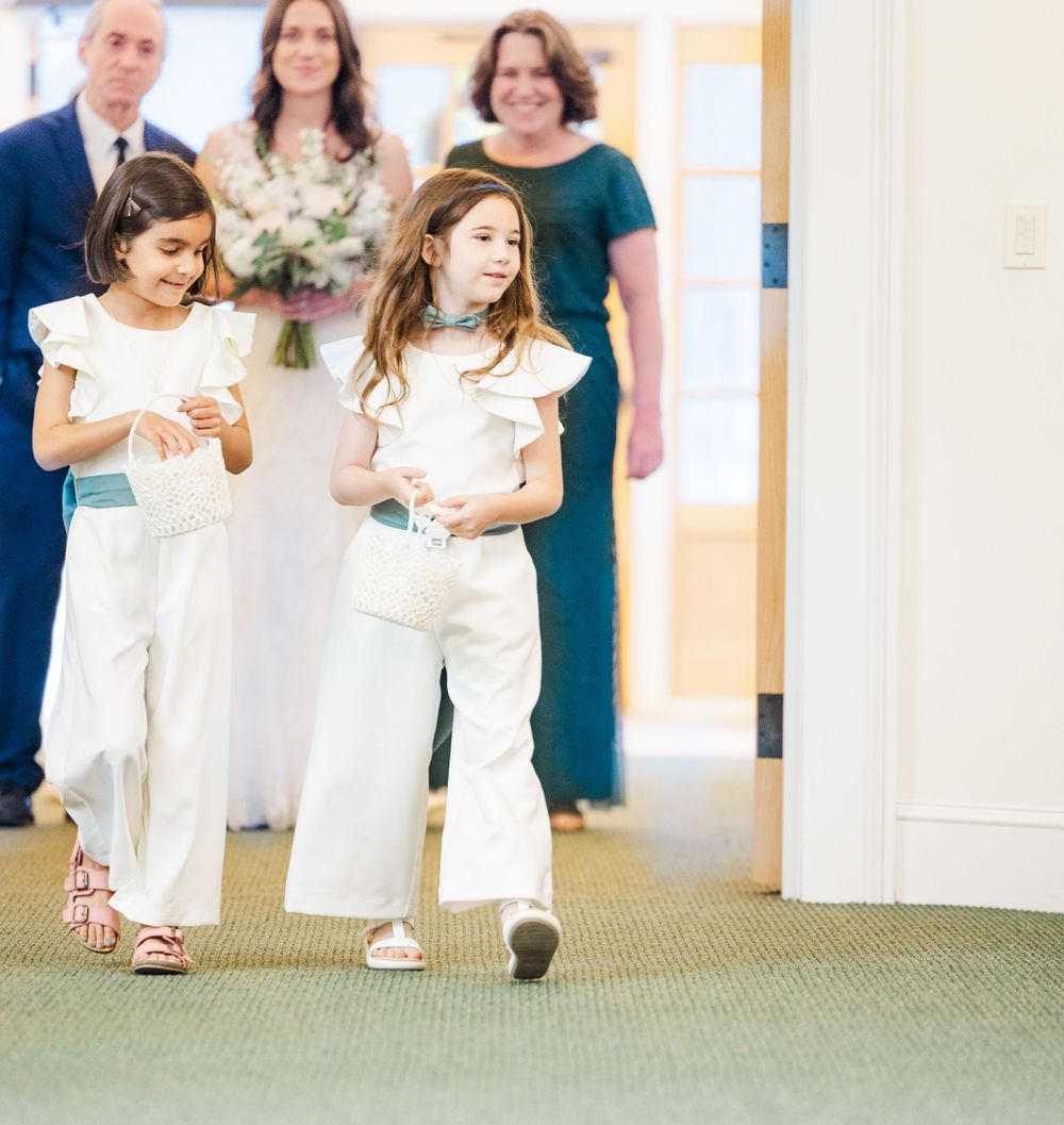 Young attendants in white outfits walking down church aisle during ceremony.