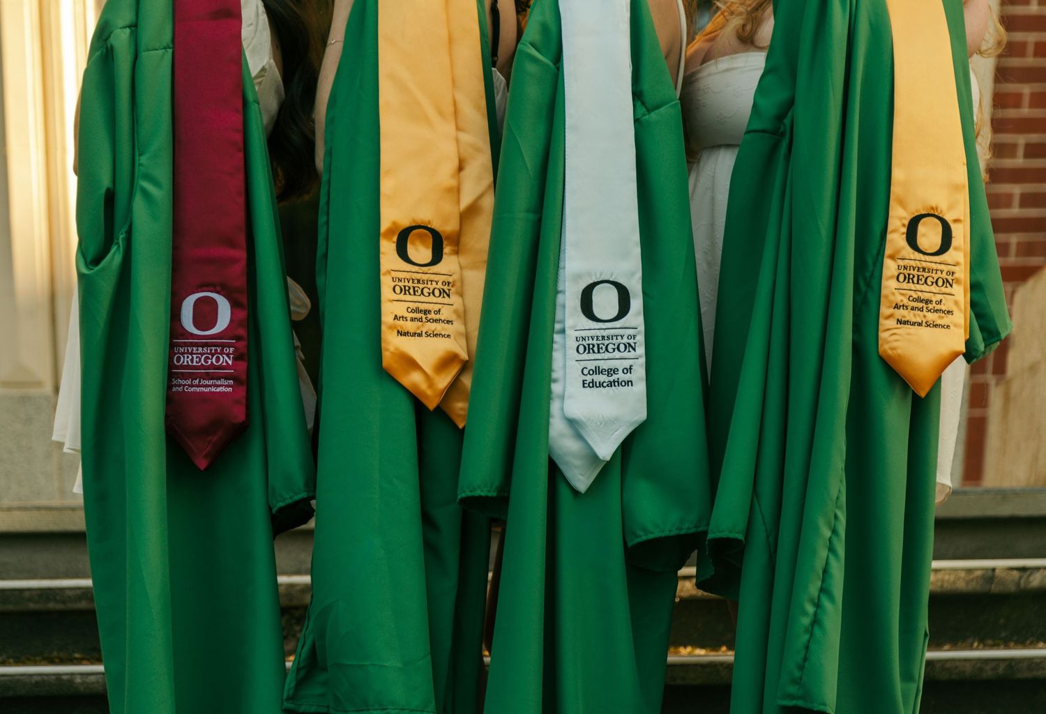 Graduate in green cap and gown facing the University of Oregon O logo in the background.