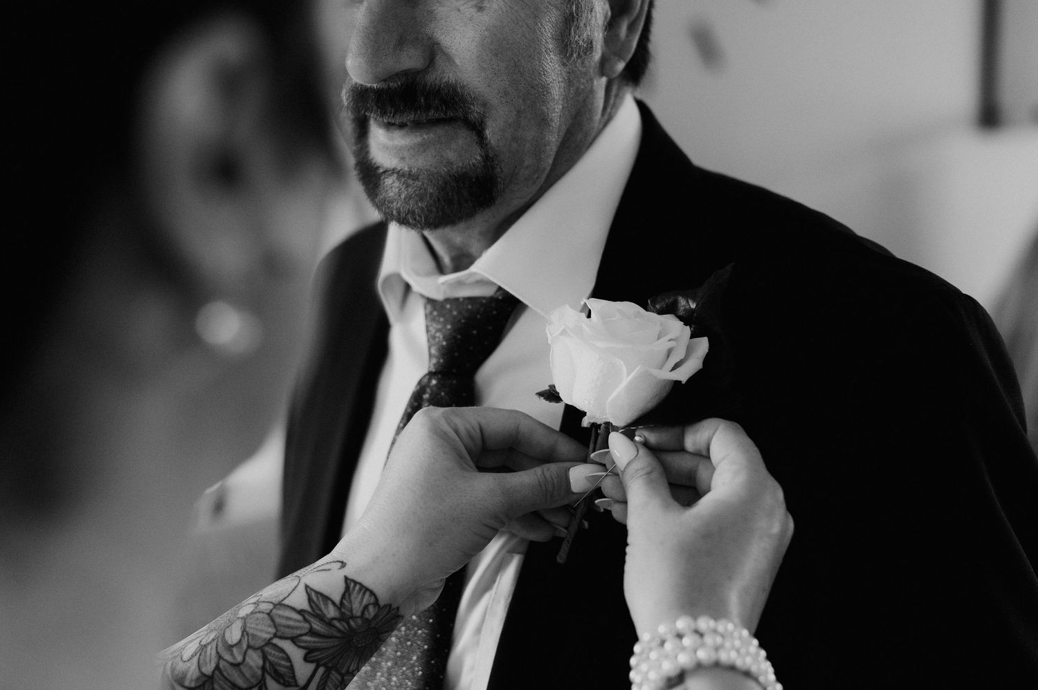 A close-up shot of hands pinning a white rose boutonniere on a formal suit.