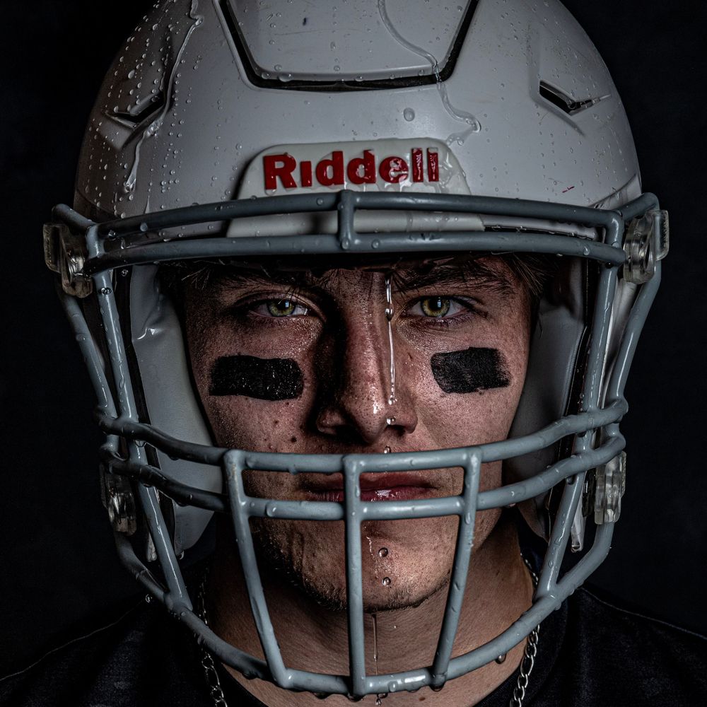 Close up of football player wearing white Riddell helmet with eye black under dramatic lighting.