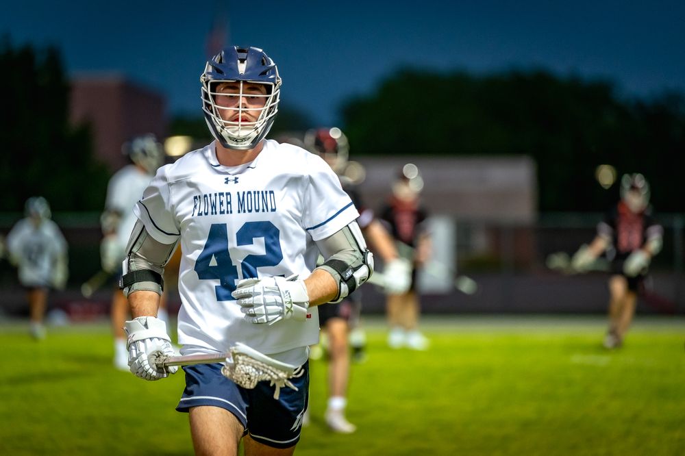 Lacrosse player in white jersey running on field during nighttime game.