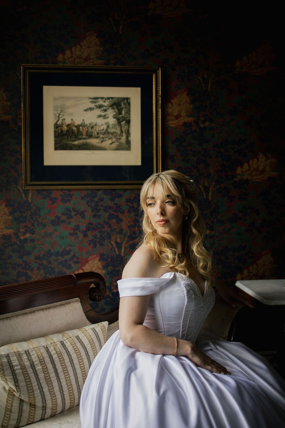 Elegant bridal portrait in a vintage-styled room with floral wallpaper and framed artwork.