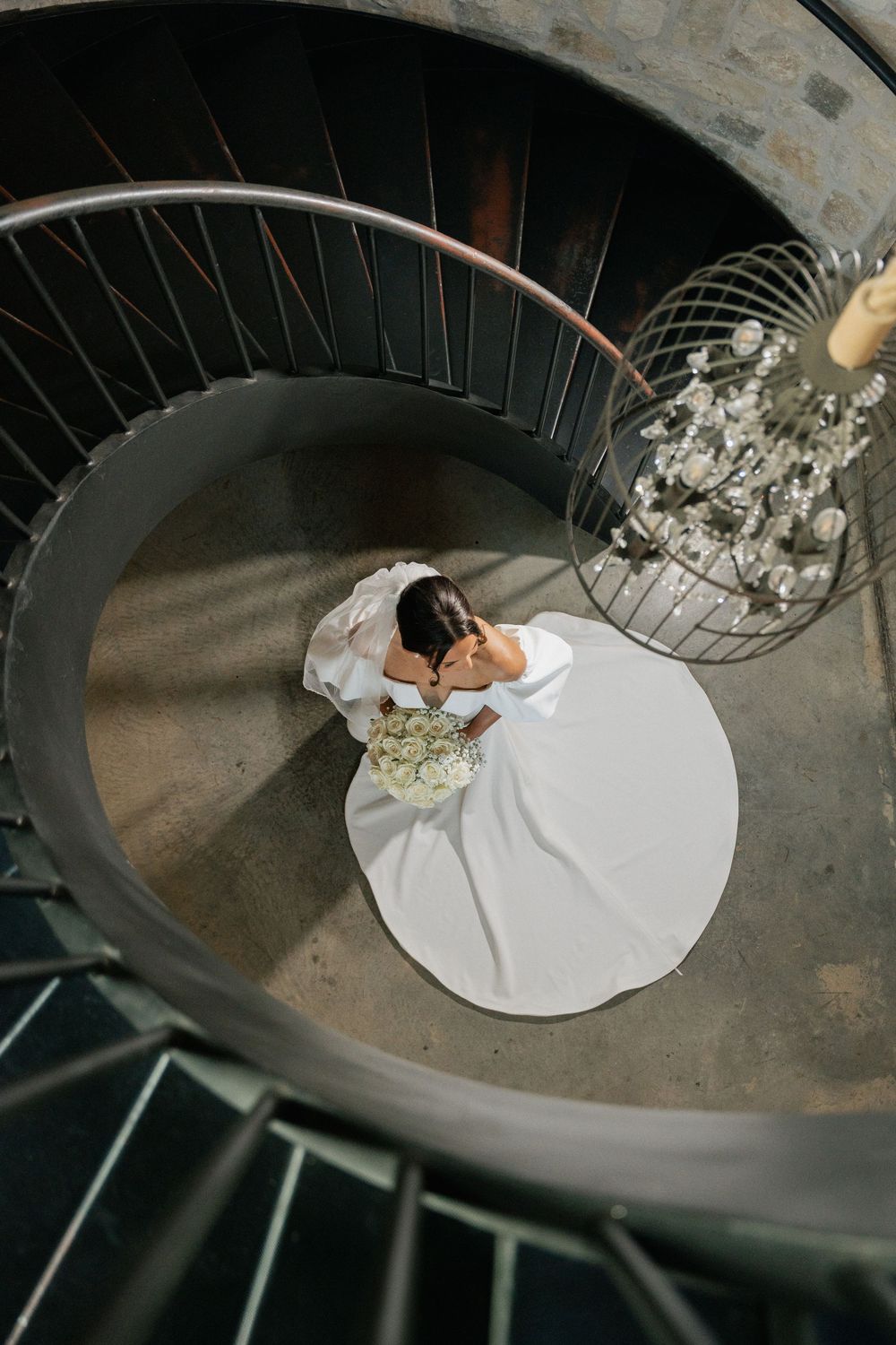 Overhead spiral staircase view showing white wedding dress and floral elements creating elegant composition.