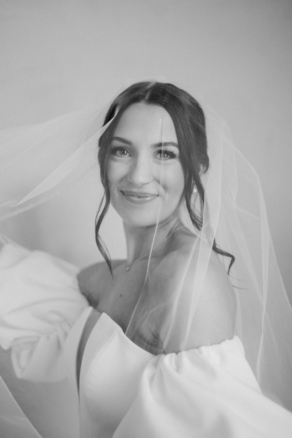 Close up portraits of bride wearing delicate white veil against light gray background.