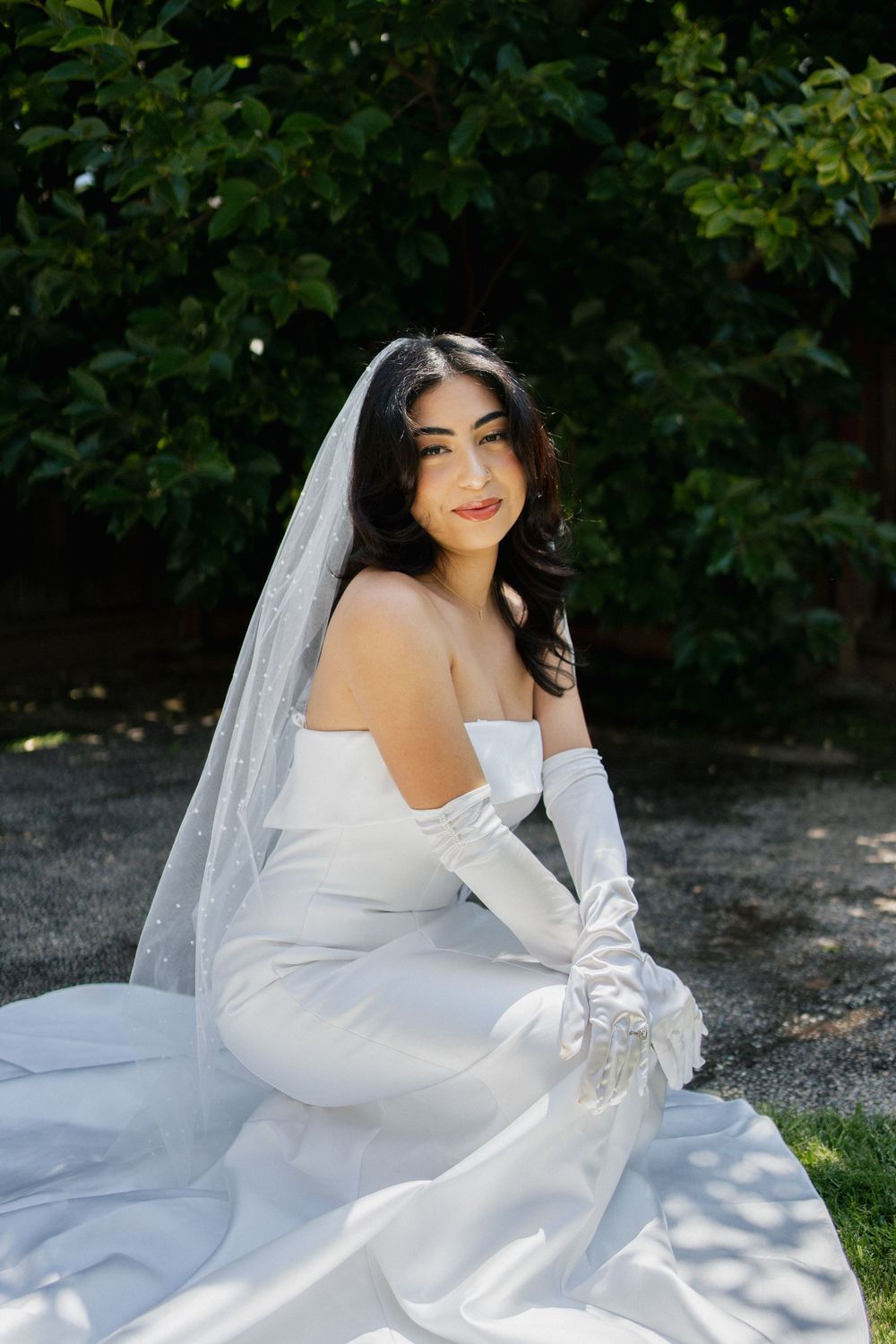 A bride in a white wedding dress with long sleeves poses gracefully outdoors against a natural background.