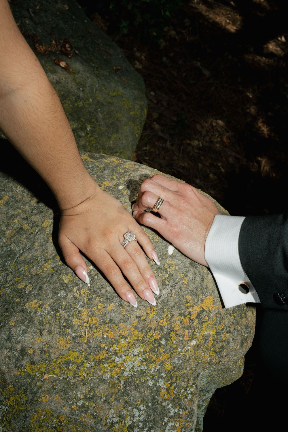 Close-up of newlywed couple's hands with wedding rings resting on a textured stone surface.