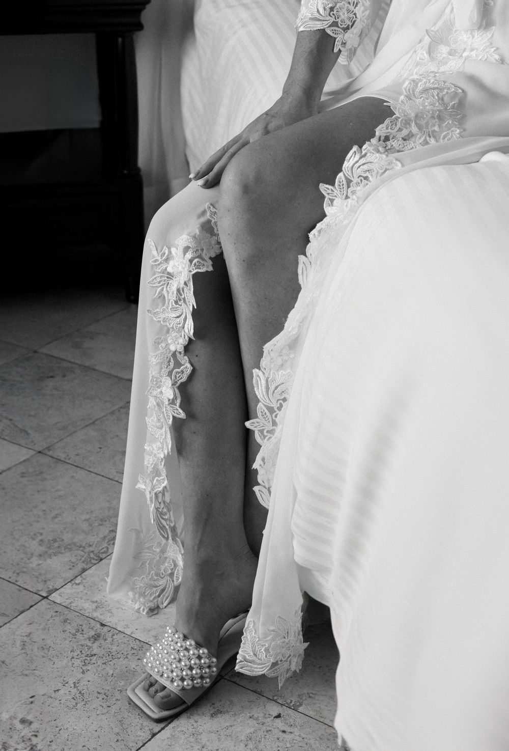 Close up black and white shot of bride's leg showing lace robe detail and studded shoe.