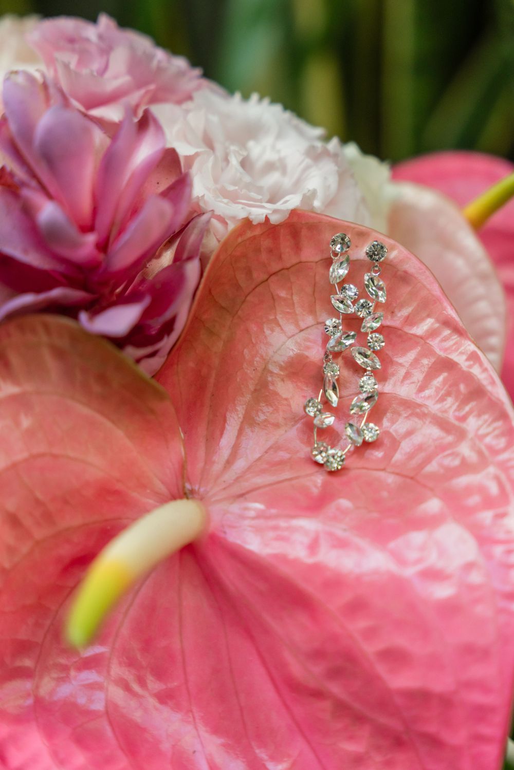 Crystal earrings placed on a pink anthurium flower with floral backdrop.