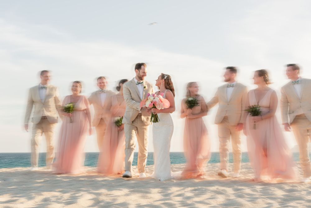 Wedding party lined up on beach in soft focus with bridesmaids in pink dresses.