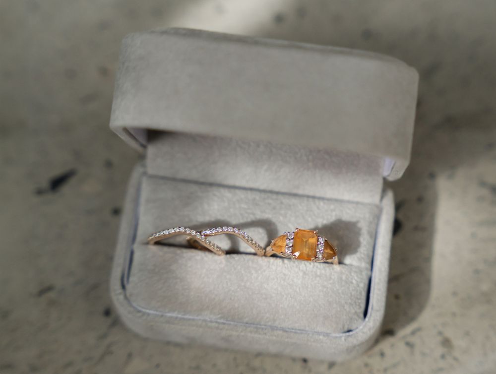 Elegant engagement ring with orange stones displayed in a grey velvet box.