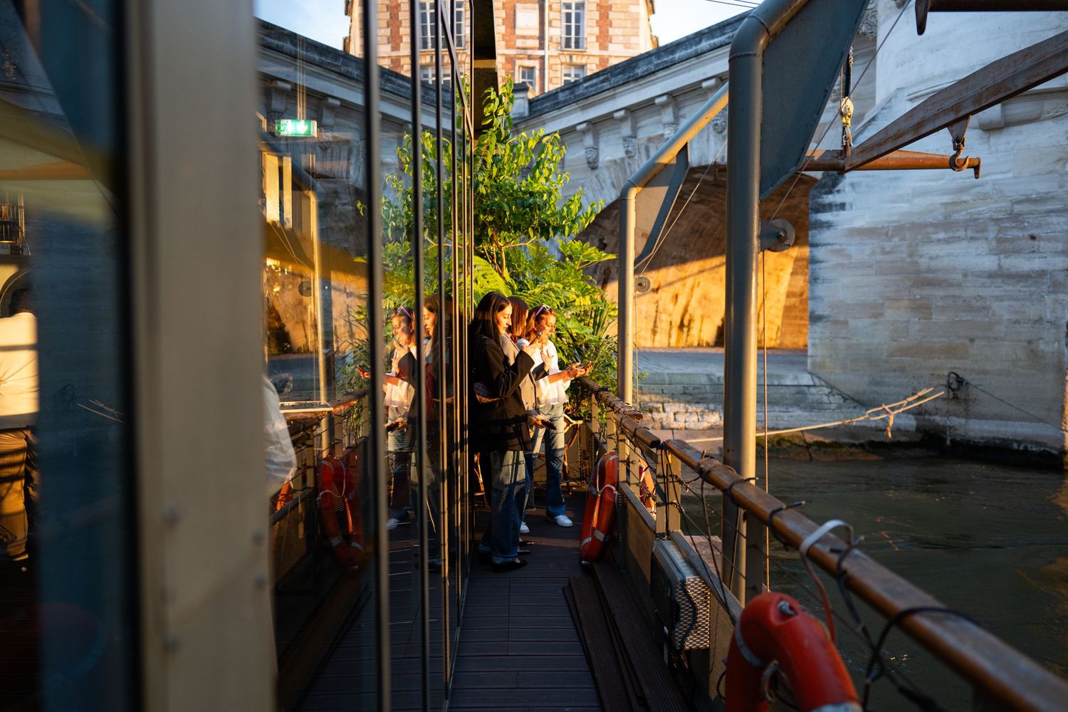 People gather on a covered outdoor walkway with late afternoon sunlight casting warm shadows.