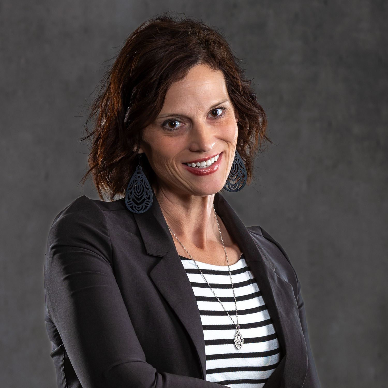 Professional headshot featuring a striped shirt and dark blazer against a grey backdrop.