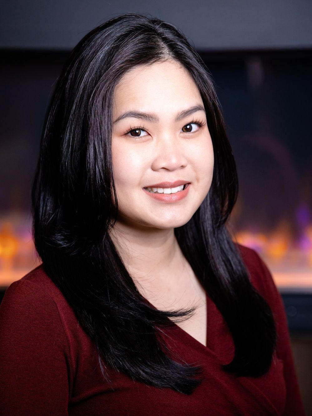 Professional headshot of someone wearing a burgundy top against a blurred cityscape background.