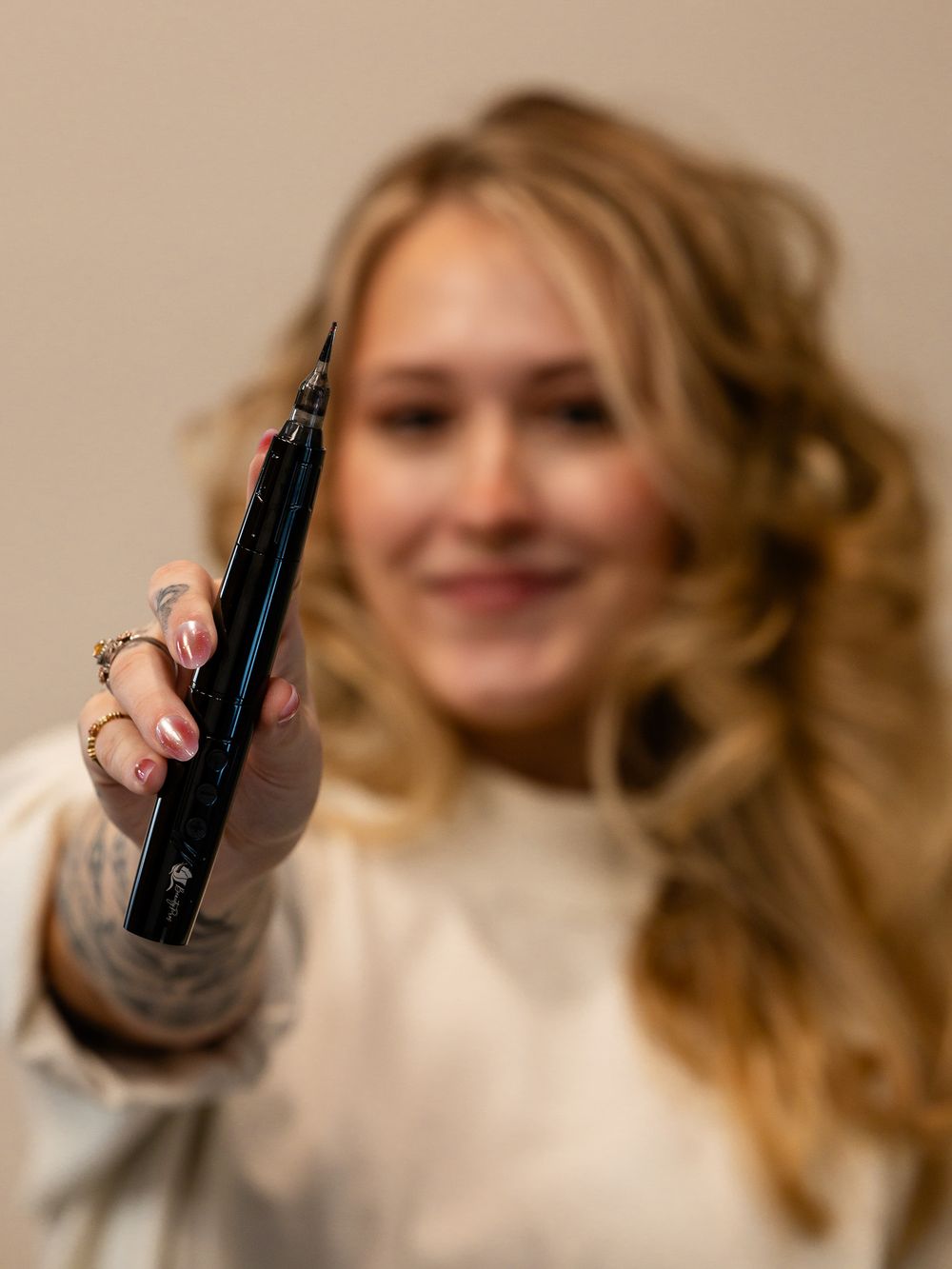 Person with wavy blonde hair holding up a black vaping device while smiling.
