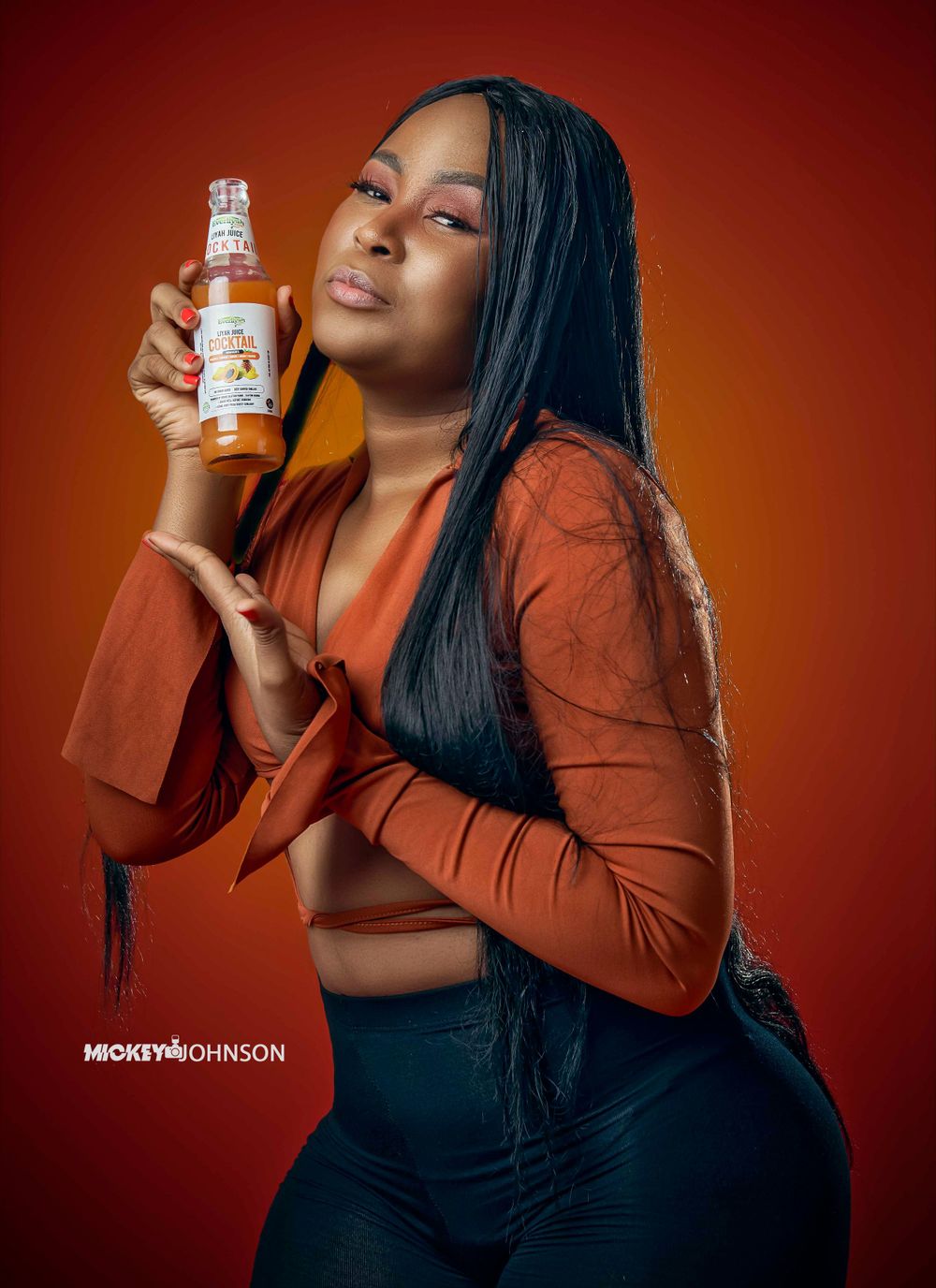 Stylish product photography featuring person with orange juice bottle against warm background.