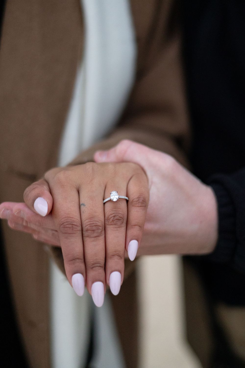Close-up of an engagement ring with a diamond solitaire on a hand with pink almond-shaped nails.