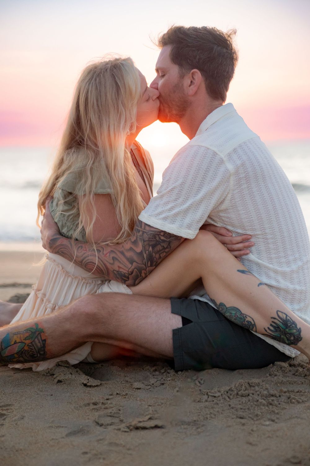Romantic couple sharing intimate moments while lying on sandy beach at sunset.