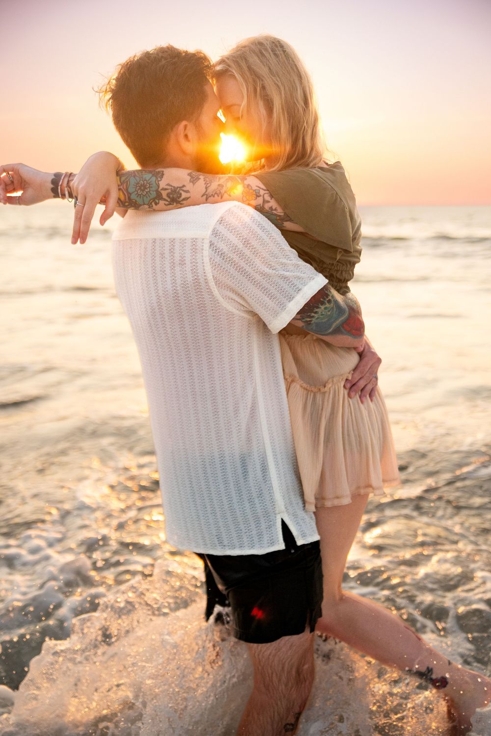A romantic couple embraces on the beach at sunset with the golden sun creating a beautiful silhouette against the ocean.