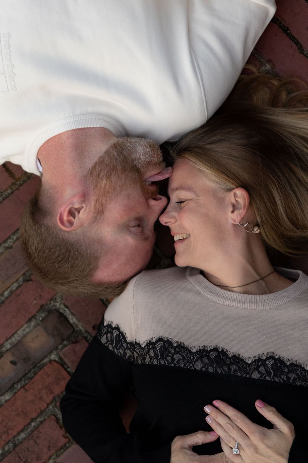 A romantic couple shares an intimate moment lying close together on brick pavement.