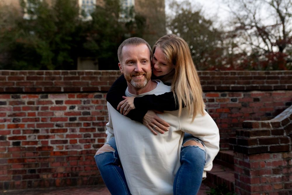A couple shares a tender moment while sitting outdoors against a brick wall background.