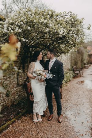 Wedding couple poses beneath flowering tree on garden path. Wedding photographer, Devon & South Hams