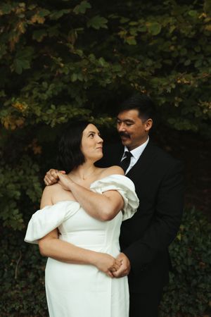 A romantic couple dances together in a garden setting, with the bride wearing a white dress and groom in dark attire.