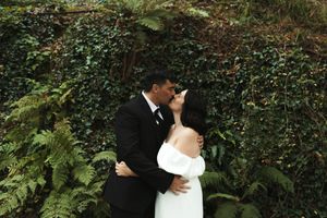 A couple in wedding attire embraces in a lush garden setting during their outdoor wedding ceremony.