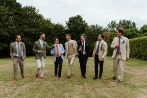 A group of people in casual suits standing together on grass with a green hedge background.