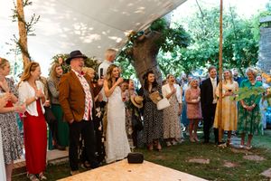 Wedding guests gather under a tent canopy to celebrate and take photos during an outdoor reception celebration.