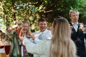 Joyful guests celebrate and toast with drinks at an outdoor garden reception party during golden hour.