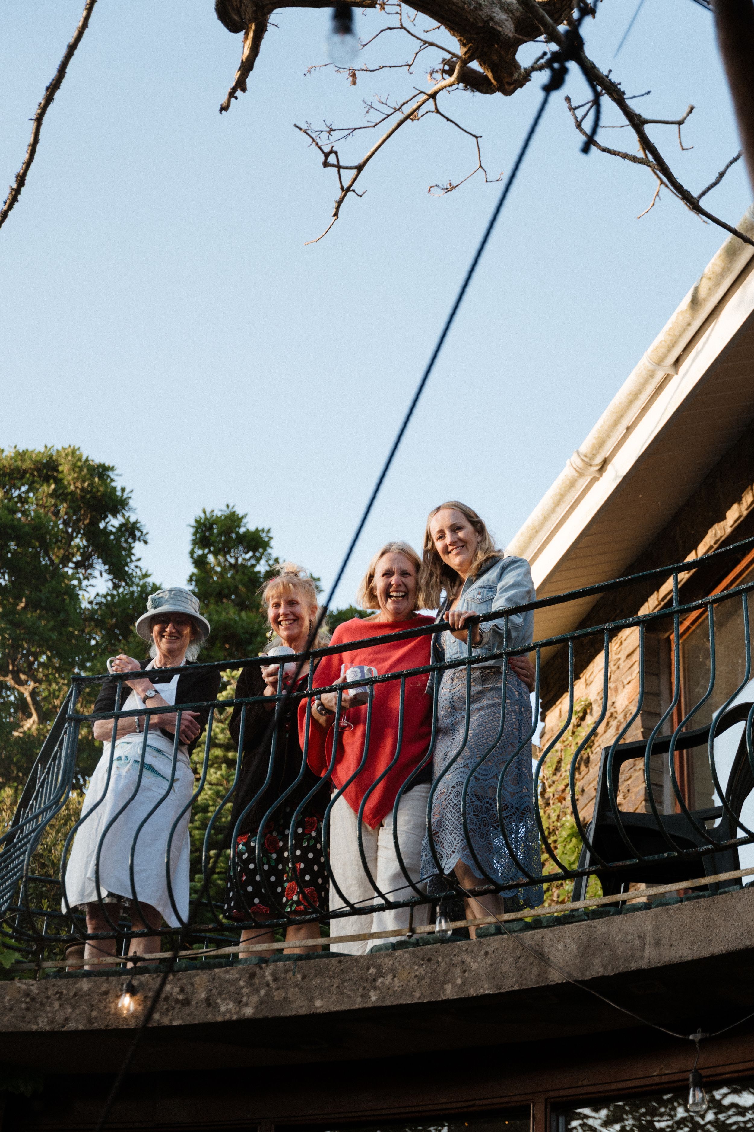 A group of seniors stands together on an outdoor balcony with ornate railings on a sunny day.