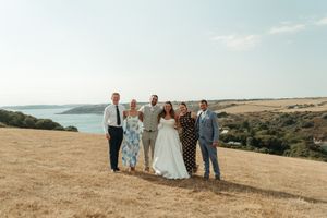 Wedding party of six posing on a golden hillside with stunning coastal views under a clear blue sky.