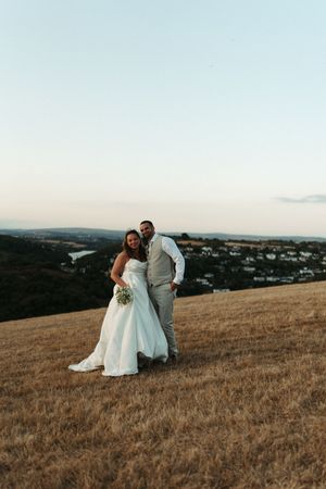 Bride and groom posing on a golden hillside at dusk with a scenic town view behind them.