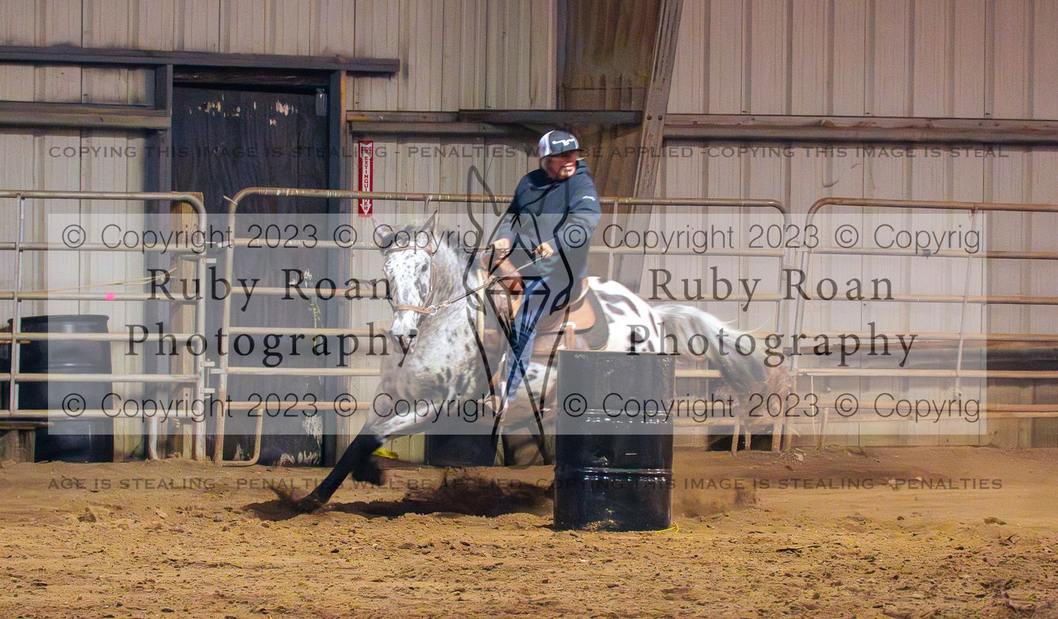 spotted horse with rider turning around black barrel