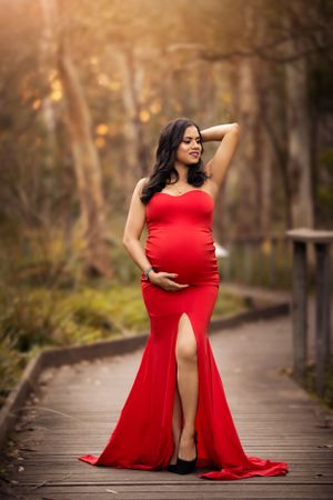 Maternity portrait of woman in form-fitting red gown on wooden boardwalk.