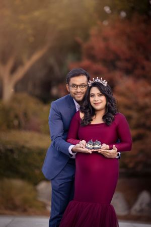 A formal portrait with burgundy dress and navy suit against autumn foliage.
