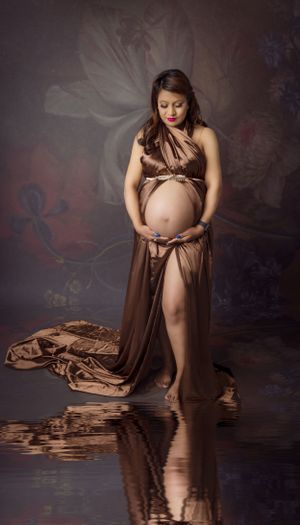 Dramatic maternity portrait in brown draped fabric against dark artistic background.