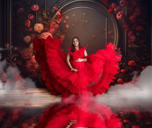 Woman in flowing red dress surrounded by roses and fog in a dramatic photo setting.
