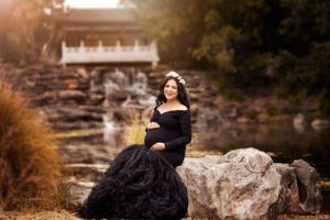 Dramatic maternity portrait in black gown near waterfall and rocks at golden hour.
