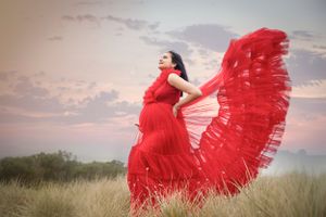 Dramatic red dress flowing in the wind against a sunset sky in an outdoor field.