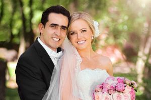Wedding portrait of newlyweds with pink bouquet in garden setting.