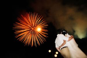 Firework bursts orange against night sky as couple dances at wedding reception.