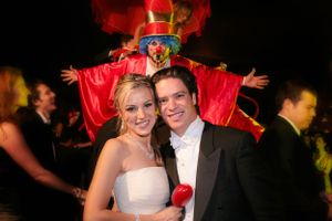 A celebratory wedding reception moment with a festive performer in red costume appearing behind the couple.